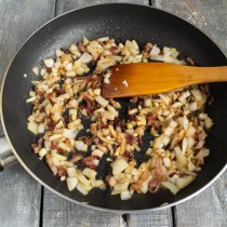 Высыпаем к бекону нарезанный лук и чеснок