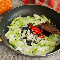 Кладём чеснок и чили в центр сковороды, обжариваем с луком
