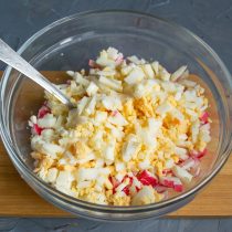Отвариваем вкрутую куриные яйца, охлаждаем, измельчаем и добавляем в салатницу