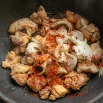Измельчаем зубчики чеснока. К обжаренной курице бросаем лук и чеснок, насыпаем красный перец