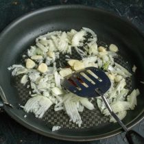 Тем временем выливаем в сковороду оливковое масло, кладём мелко нарезанный репчатый лук и чеснок, порезанный тонкими пластинками.