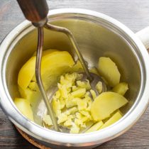 Вареный картофель разминаем толкушкой.