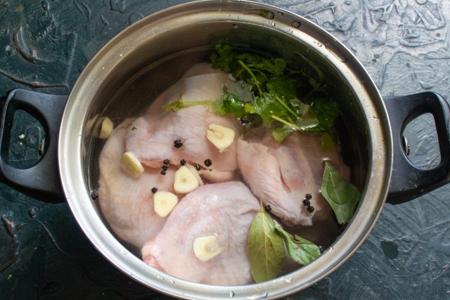 Курицу кладём в кастрюлю. Добавляем пучок кинзы вместе с корнями, чеснок, лавровый лист и горошины перца.