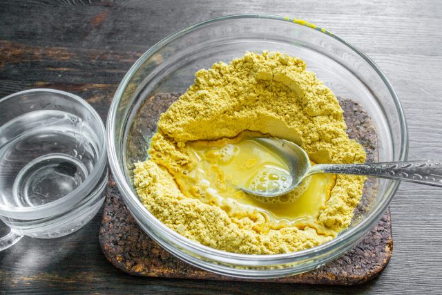 Завариваем сухую горчичную основу горячей водой. Вливаем воду температурой 70 градусов, интенсивно растираем массу ложкой, разбивая все мелкие комочки.