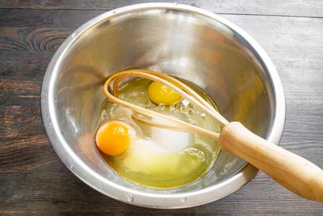 Разбиваем сырые яйца в глубокую миску, насыпаем сахарный песок и добавляем щепотку соли. Взбиваем массу миксером до получения однородного состояния.