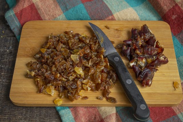 Ошпариваем кипятком изюм и финики, из последних удаляем косточки. Мелко нарезаем сухофрукты ножом Ошпариваем кипятком изюм и финики, из последних удаляем косточки. Мелко нарезаем сухофрукты ножом