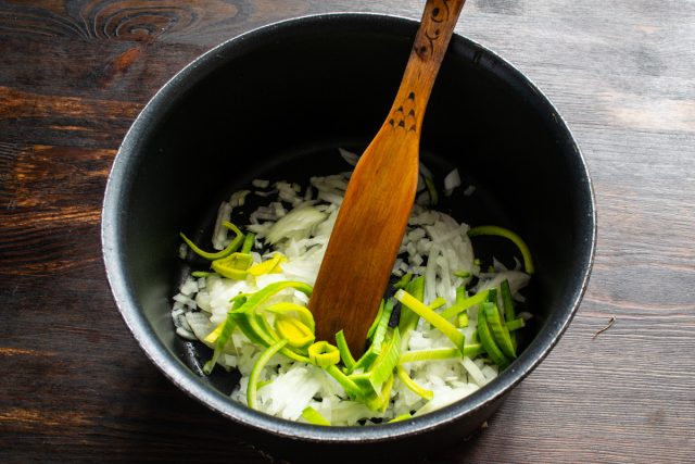 В кастрюле с толстым дном разогреваем масло. Нарезаем репчатый лук кубиками, а порей — полукольцами.