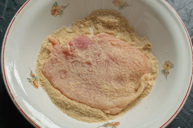 Насыпаем панировочные сухари в широкую емкость. Тщательно обваливаем каждую отбивную со всех сторон, создавая плотный слой для хрустящей корочки.