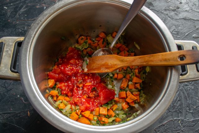 Нарезаем очищенную морковь кубиками и отправляем к луку. Через пять минут добавляем размятые консервированные томаты и тушим массу десять минут. Нарезаем очищенную морковь кубиками и отправляем к луку. Через пять минут добавляем размятые консервированные томаты и тушим массу десять минут.