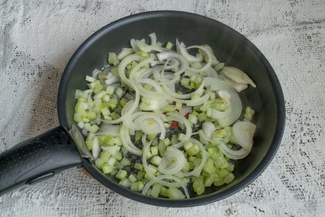 Нарезаем сельдерей кубиками, лук — полукольцами. Пассеруем овощи на оливковом масле в сковороде семь минут до появления золотистого оттенка и мягкости.