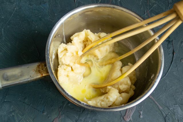 Кипятим воду с маслом и солью, всыпаем муку и завариваем тесто. Остужаем массу до 80 градусов и по одному вмешиваем яйца до получения вязкой текстуры.