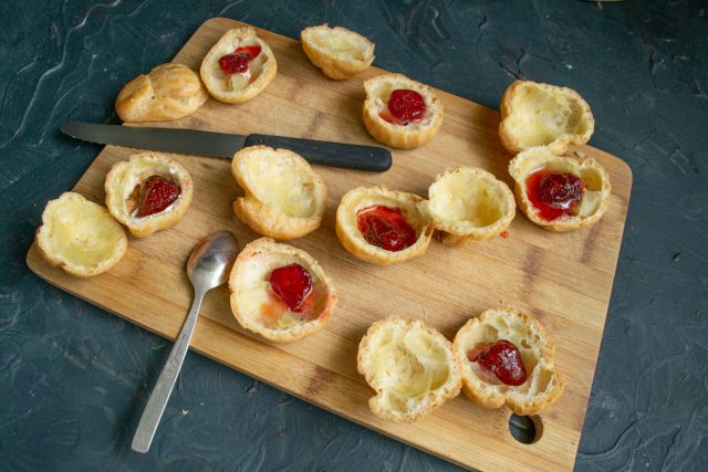 Кладем на дно нижней половинки профитроля целую ягоду клубники из варенья. Поливаем основу небольшим количеством сладкого ягодного сиропа для вкуса.