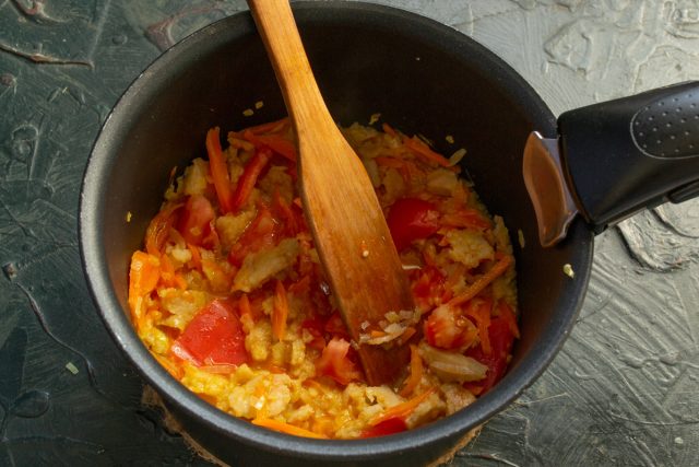 : Нарезаем крупный помидор кубиками и отправляем в кастрюлю. Обжариваем массу десять минут при постоянном помешивании, разбивая лопаткой комки рыбного фарша.