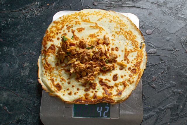 Раскладываем готовые блины на доске. В центр каждого изделия выкладываем примерно 50 граммов куриной начинки для последующего сворачивания.