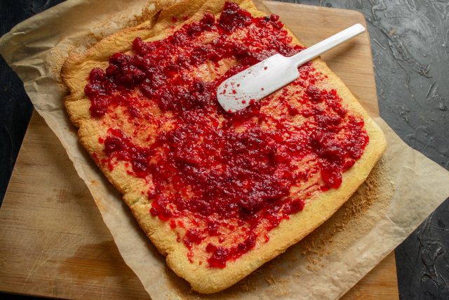 Нанесение малинового джема на развернутый бисквит