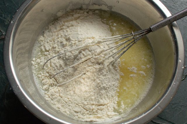 Просеиваем пшеничную муку к жидким ингредиентам и замешиваем тесто. Для удаления комочков используем погружной блендер или процеживаем массу через мелкое сито.