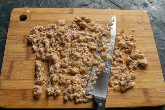 Извлекаем свиную тушенку из банки и мелко рубим мясо ножом. При желании добавляем к мясной основе предварительно обжаренный до мягкости репчатый лук.