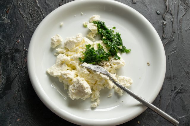 Мелко режем петрушку и растираем в ступке с солью и маслом. Добавляем полученную зеленую заправку к мягкому творожному сыру для создания ароматной основы.