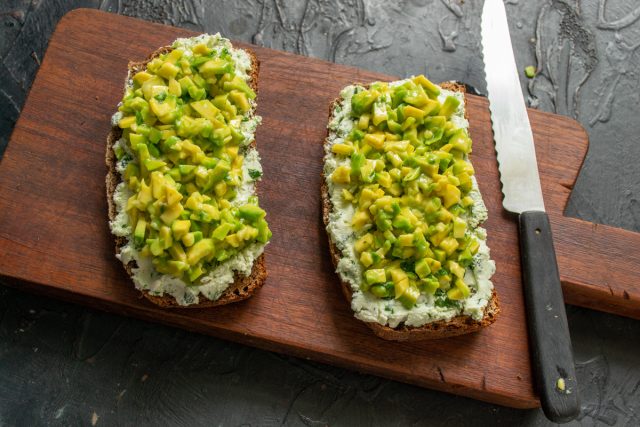 Выкладываем на слой творожного сыра приправленные кубики авокадо. Равномерно распределяем начинку внутри сырных бортиков по всей площади ломтика хлеба.