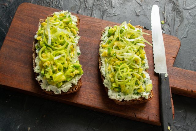 Режем лук-порей тонкими колечками и украшаем ими поверхность бутербродов. Добавляем овощные кольца для придания закуске свежести и легкой пикантности.