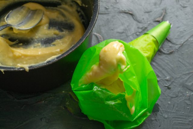 Готовое заварное тесто перекладывается в кондитерский мешок с установленным фигурным наконечником для последующего формирования заготовок пирожных на противне.