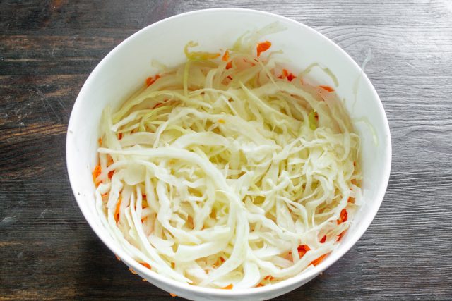 Шинкуем капусту тонкими полосками и разминаем руками до мягкости. Выкладываем ровно половину подготовленной капусты в форму вторым слоем поверх моркови и лука.