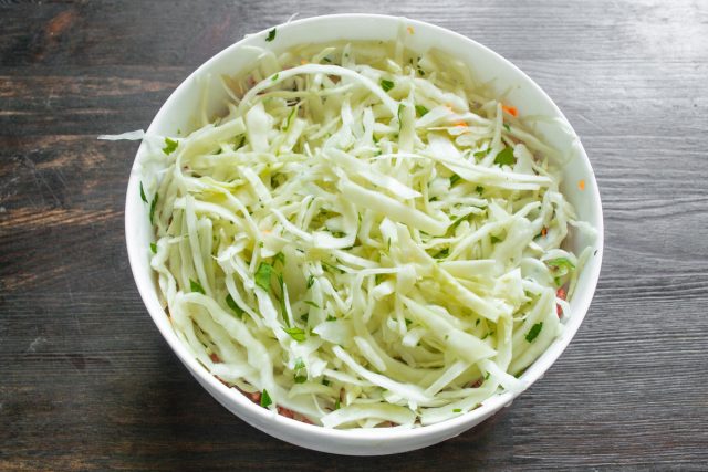 Мелко рубим зелень петрушки и укропа, смешиваем ее с остатками нашинкованной капусты. Выкладываем финальный капустный слой, полностью закрывая мясную начинку.