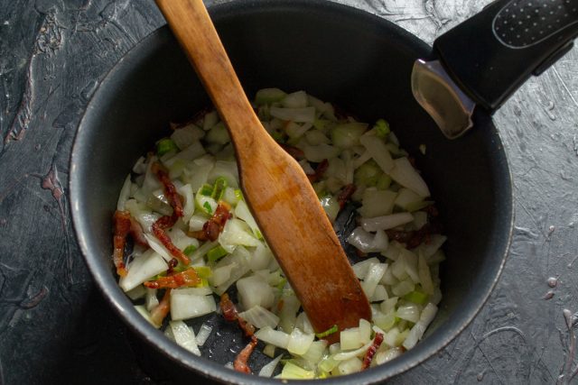 Шинкуем репчатый лук и порей мелкими кусочками, отправляем к поджаренному бекону. Пассеруем овощи до полупрозрачности, периодически помешивая массу лопаткой.