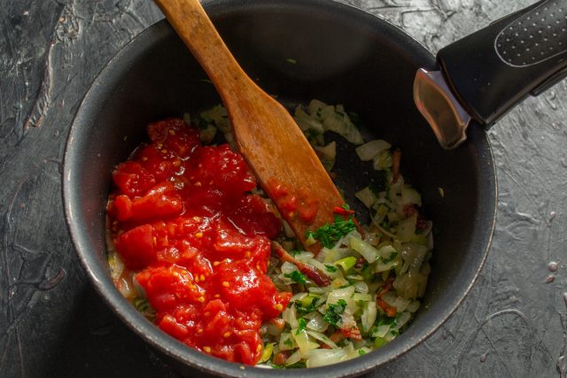 Выкладываем в кастрюлю резанные консервированные томаты в собственном соку. Если используете свежие помидоры, предварительно очистите их от кожицы и мелко нарежьте.