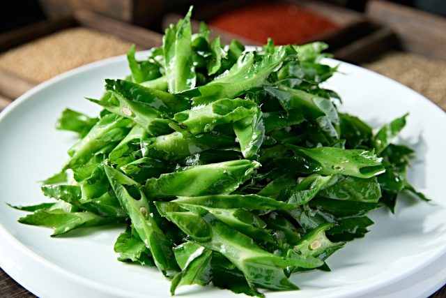 Нарезанные свежие зеленые стручки четырехкрыльника пурпурного на белой тарелке