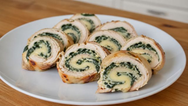 Куриное филе, свернутое с начинкой из шпината и сыра. При нарезке видна плотная спираль и сочная текстура внутри.