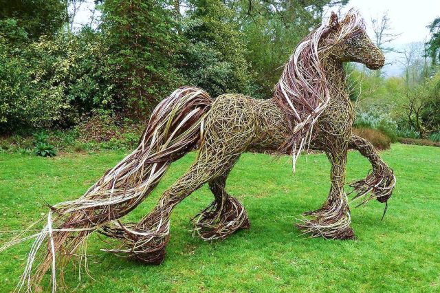 Необычный садовый декор в виде плетеного коня из гибких прутьев на зеленом газоне