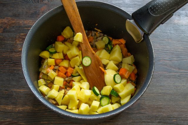 Нарезанный кубиками картофель и кружочки цуккини засыпаются в кастрюлю к овощам