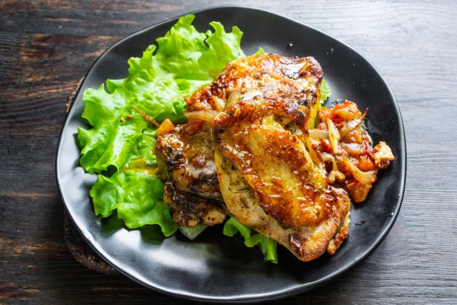 Готовое блюдо из курицы перед подачей Жареные куриные бедра с луком и помидорами на тарелке с салатными листьями