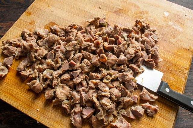Нарезка вареных куриных желудков на небольшие кусочки на доске