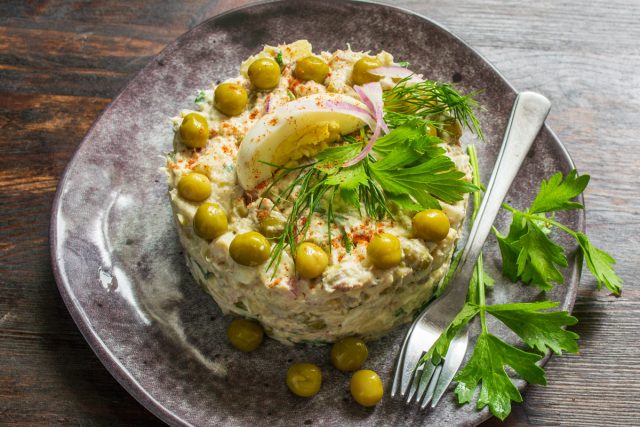 Снятие кулинарной формы. Металлическое кулинарное кольцо аккуратно снимают с готового круглого салата на тарелке.