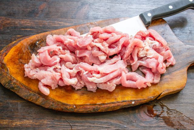 Подготовка свинины для мясного рагу Нарезка свинины тонкими полосками на доске