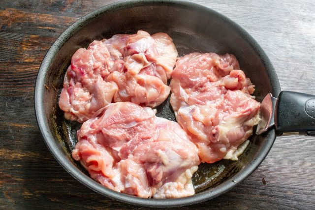 Обжаривание куриного мяса на сковороде. Куриные бедра обжариваются кожей вниз на раскаленной глубокой сковороде.