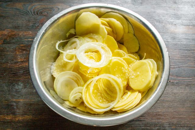 Очищенный картофель нарезаем тонкими кружочками и кладем в миску. Добавляем оставшийся лук, соль и поливаем маслом. Тщательно перемешиваем, покрывая каждый ломтик картошки.