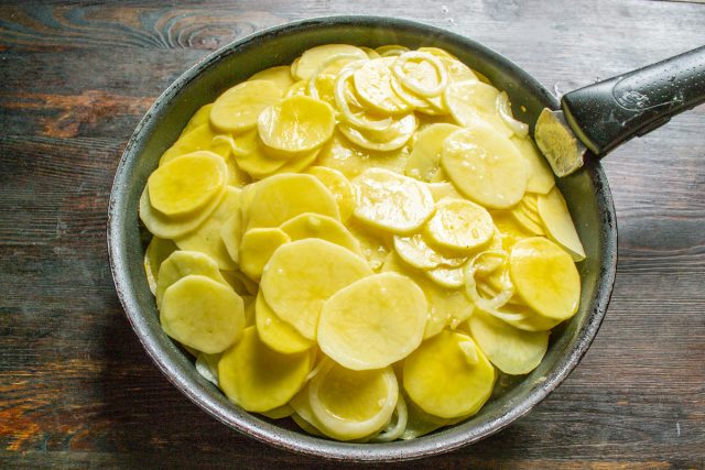 Аккуратно выкладываем подготовленные ломтики картошки на обжаренное мясо внахлест. В процессе формирования гарнира у нас должно получиться сразу несколько ровных слоев.