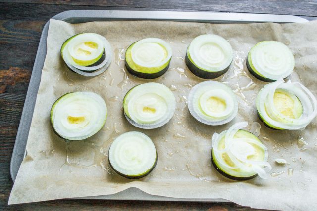 Нарезаем репчатый лук очень тонкими аккуратными колечками и аккуратно выкладываем их сверху на кружочки баклажанов, равномерно распределяя по всей поверхности.