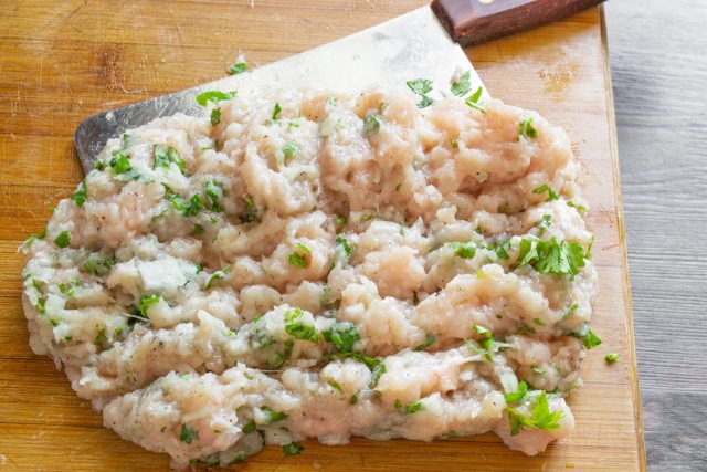 Посыпаем куриное филе с зеленью солью и молотым черным перцем, а затем тщательно рубим массу тяжелым мясным топориком прямо на деревянной доске до получения однородного фарша.