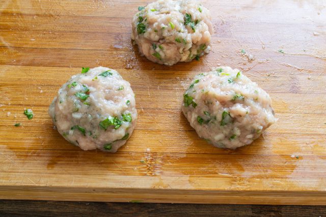 Разделяем приготовленный рубленый куриный фарш со специями и зеленью на три абсолютно равные порции и смачиваем ладони водой, после чего лепим аккуратные круглые плоские котлеты.
